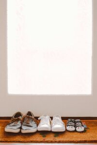 A collection of family shoes, including baby booties, on a welcoming mat by the door.