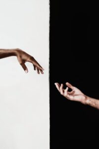 Two hands reaching across a stark black and white divide, symbolizing connection and unity.